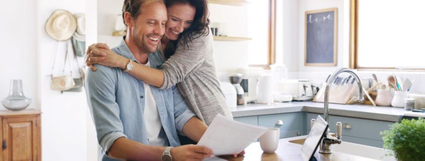 wife hugging her husband in the kitchen while the husband views homeowner insurance options