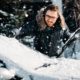 Man clearing snow off car windshield during heavy snowfall in winter